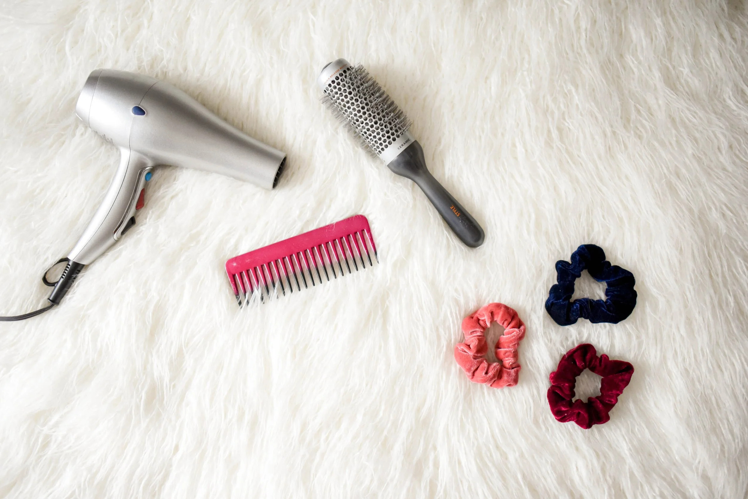 Hair dryer, round brush, comb, and hair ties arranged on a light surface